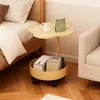 A bedside table with a flower-shaped top and a storage basket on wheels, placed next to a bed and a sofa. Produktbild-Vorschau