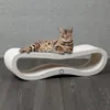 A Bengal cat is lying on a white, curved scratching board. Produktbild-Vorschau