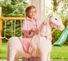 A young girl is playing with a white toy horse with a pink saddle in a backyard setting. Anteprima dell’immagine prodotto