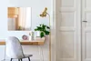 A modern home office setup with a desk, chair, lamp, and a mirror on the wall. Produktbild-Vorschau