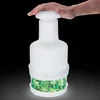 A hand presses down on the lid of a white manual food chopper filled with chopped green vegetables. Náhled obrázku produktu