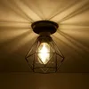 A close-up shot of a vintage-style ceiling light fixture with a diamond-shaped metal cage and an exposed Edison bulb, casting dramatic shadows on a textured ceiling. Produktbild-Vorschau
