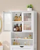 A white storage cabinet with glass doors filled with various bottles and jars. Náhled obrázku produktu
