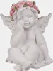 A white cherub figurine with a pink rose wreath on its head sits with its legs crossed. Produktbild-Vorschau