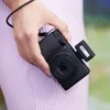 A hand holding a black camera with a small flash attachment. Podgląd zdjęcia produktu