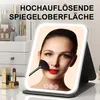 A woman applying makeup using a lighted mirror, with makeup products in the background. Produktbild-Vorschau