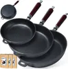 A set of three cast iron frying pans of varying sizes, with dark wooden handles, are arranged in a staggered formation against a white background. Two cardboard boxes are visible in the bottom left corner. Voir les images du produit