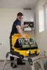 A technician is working on a boiler, with a tool case on a step ladder. Voir les images du produit