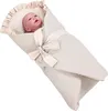 A baby doll wrapped in a beige swaddle blanket with a ribbon bow. Produktbild-Vorschau