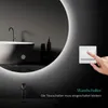 A hand is shown pressing a light switch next to a large, illuminated round mirror in a modern bathroom setting. A bathtub is visible in the reflection. Voir les images du produit