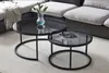 A set of two round coffee tables with black metal frames and glass tops, placed in a living room setting next to a sofa. Náhľad obrázku produktu