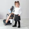 A young girl is standing next to a toy cleaning cart with a vacuum cleaner. Produktbild-Vorschau