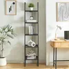 A tall, black ladder shelf unit with five shelves, decorated with various items, stands against a white wall next to a desk with a lamp and laptop. Anteprima dell’immagine prodotto