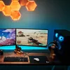 A gaming setup with two monitors, a computer tower, keyboard, mouse, and headphones, illuminated by hexagonal wall lights and LED strip lighting. Produktbild-Vorschau