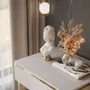 A close-up of a decorative bust and dried flowers on a table next to a window with curtains. Produktbild-Vorschau