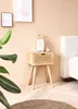 A bedside table with a drawer and rattan front is placed next to a bed in a bedroom setting. A plant is in the foreground. Produktbild-Vorschau
