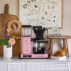 A pink Moccamaster coffee maker is displayed on a kitchen counter, with flowers and croissants nearby. Náhľad obrázku produktu