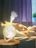 A child sleeping in bed with a moon-shaped humidifier emitting mist. Podgląd zdjęcia produktu