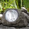 A solar-powered garden light disguised as a rock, placed among plants and other rocks. Produktbild-Vorschau
