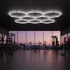 A modern gym with large windows overlooking a city skyline at dusk, featuring various exercise equipment and people working out. Podgląd zdjęcia produktu