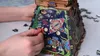 A close-up shot of a person's hands assembling a wooden puzzle box shaped like a pyramid, with colorful illustrations of fish and geometric patterns. Náhľad obrázku produktu
