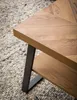 A close-up shot of a wooden coffee table with a herringbone pattern, resting on a textured rug. Voir les images du produit
