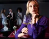 A woman in a purple dress holds a glass of white wine at a party with other people in the background. Produktbild-Vorschau