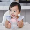 A baby sitting in a high chair and holding a sippy cup. Produktbild-Vorschau