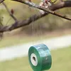 A roll of green grafting tape is hanging from a tree branch, with the tape being unrolled. Produktbild-Vorschau