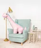 A pink dinosaur plush toy is sitting in a mint green armchair next to a floor lamp and two small side tables. Voir les images du produit