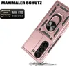 A rose gold phone case with a ring holder and camera cover is shown at an angle, with debris scattered below it, suggesting it has been dropped. Produktbild-Vorschau