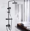 A black shower fixture set with a rainfall showerhead, handheld shower, and shelf, displayed in a modern bathroom setting with a bathtub in the background. Produktbild-Vorschau