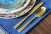 A close-up view of gold cutlery and decorative plates on a blue napkin. Podgląd zdjęcia produktu