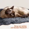 A Siamese cat is resting on a plush gray surface, with text overlay describing the material. Podgląd zdjęcia produktu
