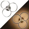 A split image showing a modern LED ceiling light with three interlocking rings. The left side shows the light fixture against a white background, while the right side shows the light fixture illuminated against a dark brown background. Podgląd zdjęcia produktu