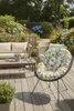 A comfortable outdoor seating area with a sofa, coffee table, and a patterned chair, surrounded by lush garden greenery and hydrangeas. Produktbild-Vorschau