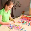 A young girl is sitting at a table and creating crafts with colorful pipe cleaners and small toy dinosaurs. Produktbild-Vorschau