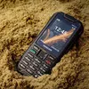 A rugged Maxcom phone is partially buried in sand. Podgląd zdjęcia produktu