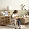 A young girl wearing headphones is sitting in a rocking chair, looking at her phone. She is holding a stuffed animal. In the background, there is a mushroom-shaped humidifier with a purple light, a white horse figurine, a lamp, and a clock on the wall. Ano Voir les images du produit
