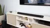 A soundbar and subwoofer are placed on a media console below a television, with decorative items and video game controllers also present. Produktbild-Vorschau