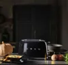 A black SMEG toaster is displayed on a countertop with a pumpkin and a bowl of soup, suggesting a cozy, autumnal setting. Náhľad obrázku produktu