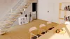A modern interior scene featuring a staircase, a bookshelf, and a dining area with chairs and a table. Náhled obrázku produktu