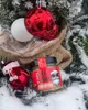 A jar of Eierlikör is placed in the snow next to a Christmas tree decorated with ornaments and a burlap bag. Produktbild-Vorschau