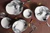 A collection of plates with a marbled design, arranged on a brown surface with decorative elements like cinnamon sticks and bay leaves. Anteprima dell’immagine prodotto