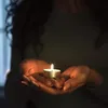 A person holding a lit candle in their hands. Náhled obrázku produktu