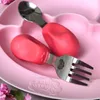 A close-up shot of a pink baby plate with a fork and spoon on it. Voir les images du produit