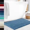 A blue bath mat is placed in front of a white bathtub. Anteprima dell’immagine prodotto