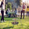People are gathered in a backyard around a tripod grill with a fire pit and cooking grate. Produktbild-Vorschau