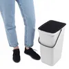 A person wearing jeans and sneakers stands next to a white trash can with a black lid. Anteprima dell’immagine prodotto