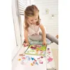 A young girl is playing with a magnetic farm-themed toy box on a windowsill. Produktbild-Vorschau